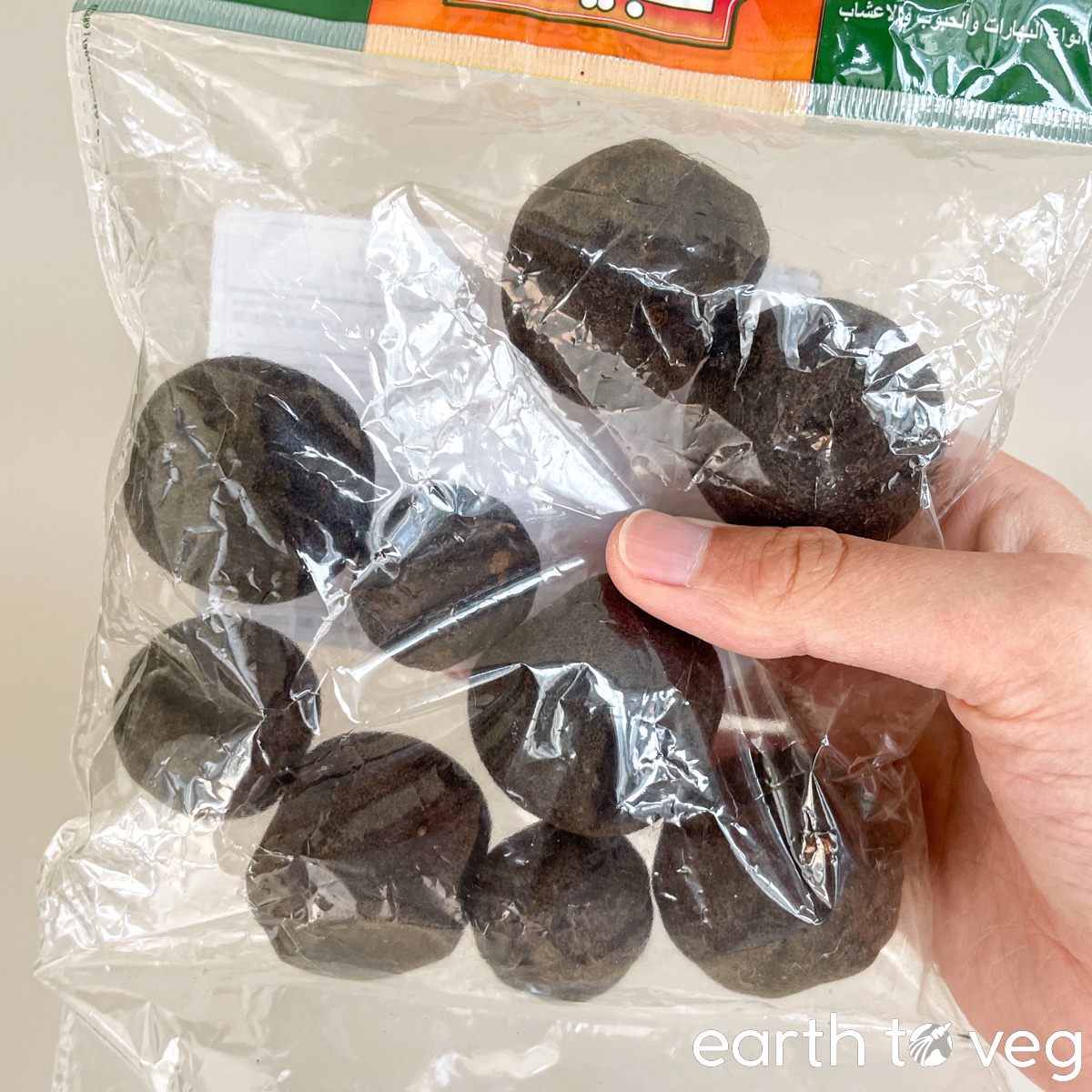 Package of dried Iranian black limes held up against a beige background.