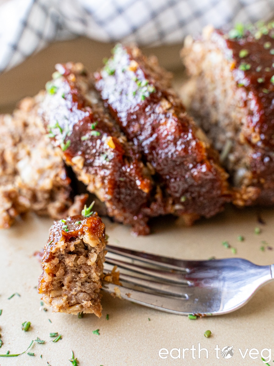 Sliced vegan meatloaf on a baking tray, next to a fork holding a bite of meatloaf.