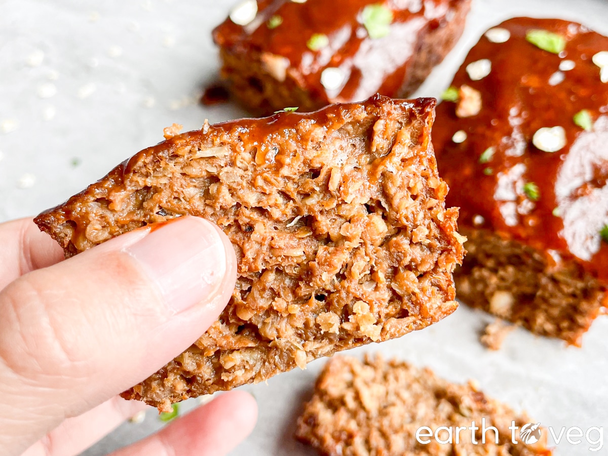 A hand holds up a small slice of Impossible Meatloaf to show its fibrous meat-like texture.