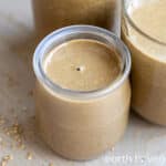 Glass jar of sesame butter on a wooden table.
