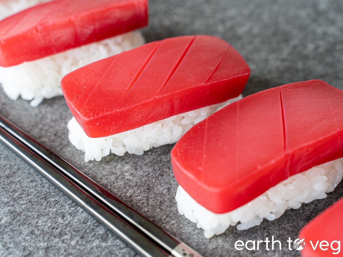 Vegan nigiri sushi and a pair of chopsticks on a grey slate board.