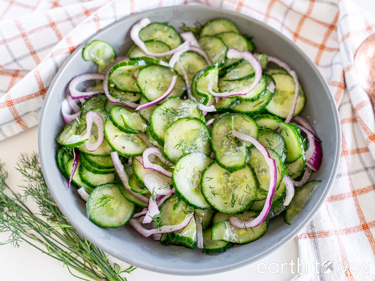 A bowl of German cucumber salad on a gingham towel.