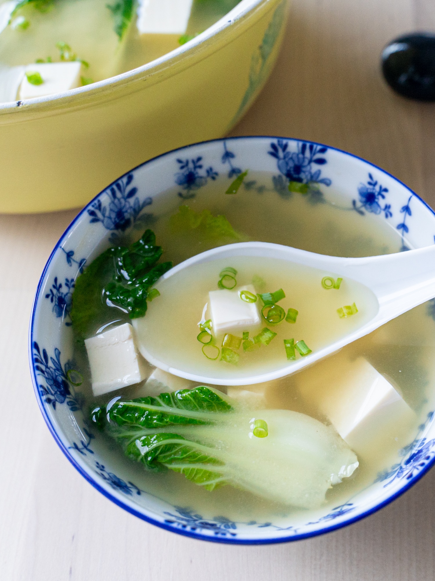 A white soup spoon rests in a small bowl full of bok choy tofu miso soup.
