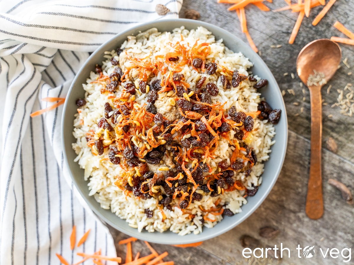 A plate of vegetarian Kabuli Pulao on a wooden table with a white striped tablecloth.