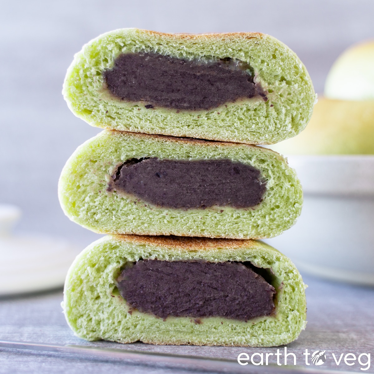 A stack of three pandan red bean buns sliced in half on a grey tabletop.