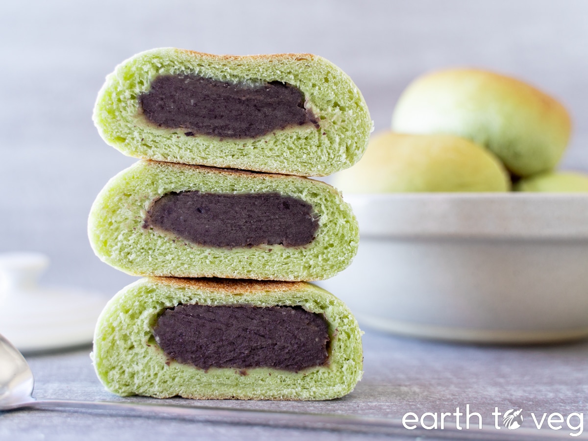 A stack of green pandan red bean buns on a grey surface.