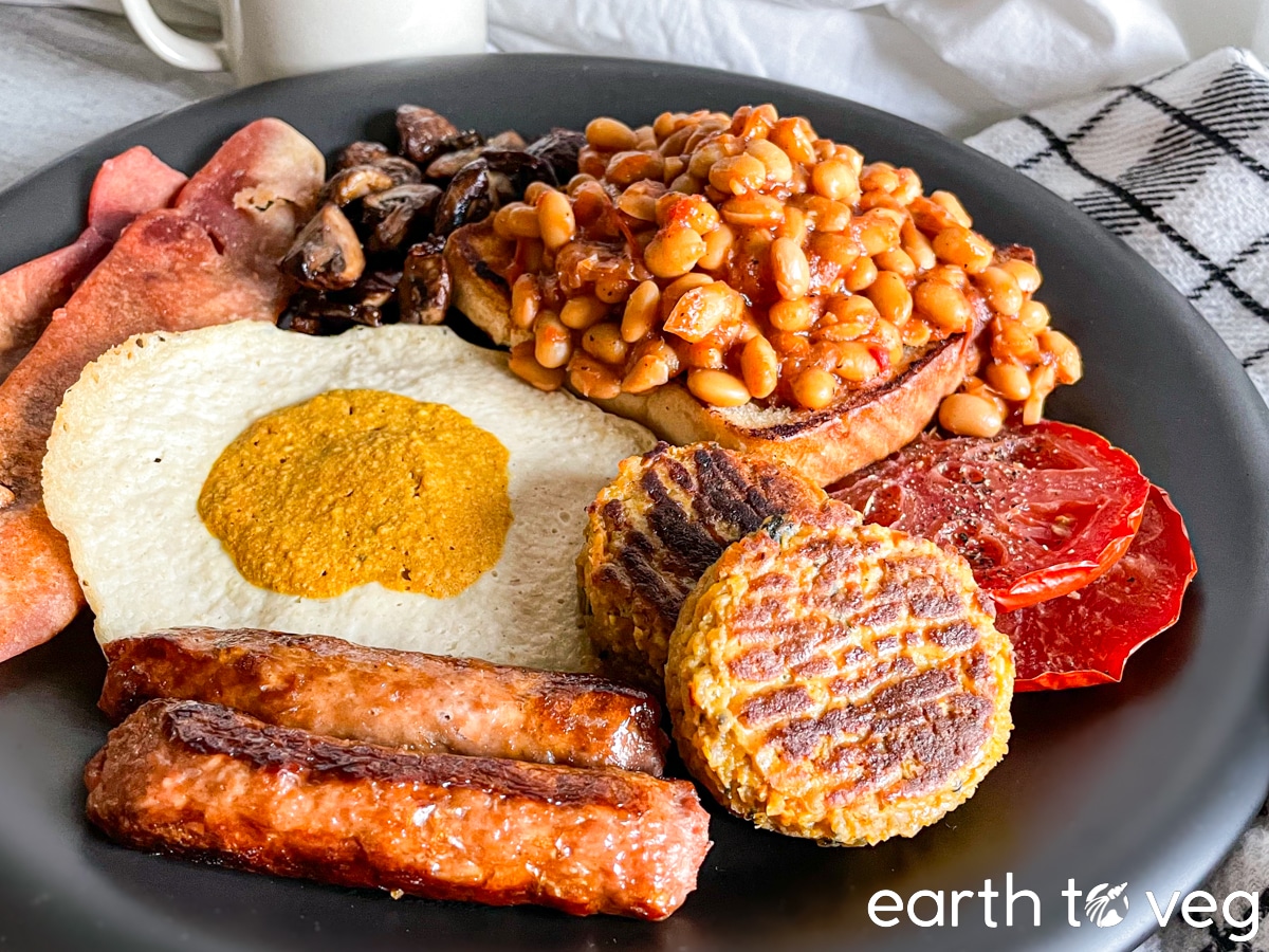 A plate of vegan full English breakfast with a mug of hot black tea in the background.