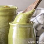 A wooden spoon scoops smooth roasted pumpkin seed butter out of a glass jar.