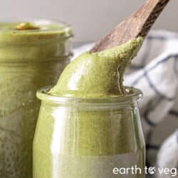 A wooden spoon scoops smooth roasted pumpkin seed butter out of a glass jar.