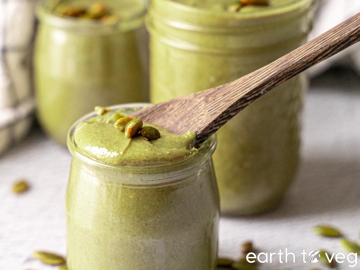 A wooden spoon scoops luscious roasted pumpkin seed butter out of a small jar.