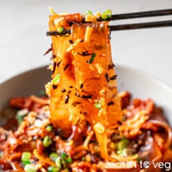 Korean buldak glass noodles lifted up by a pair of black chopsticks.
