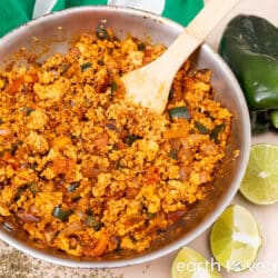 A wooden spoon stirring Chipotle tofu sofritas in a skillet.