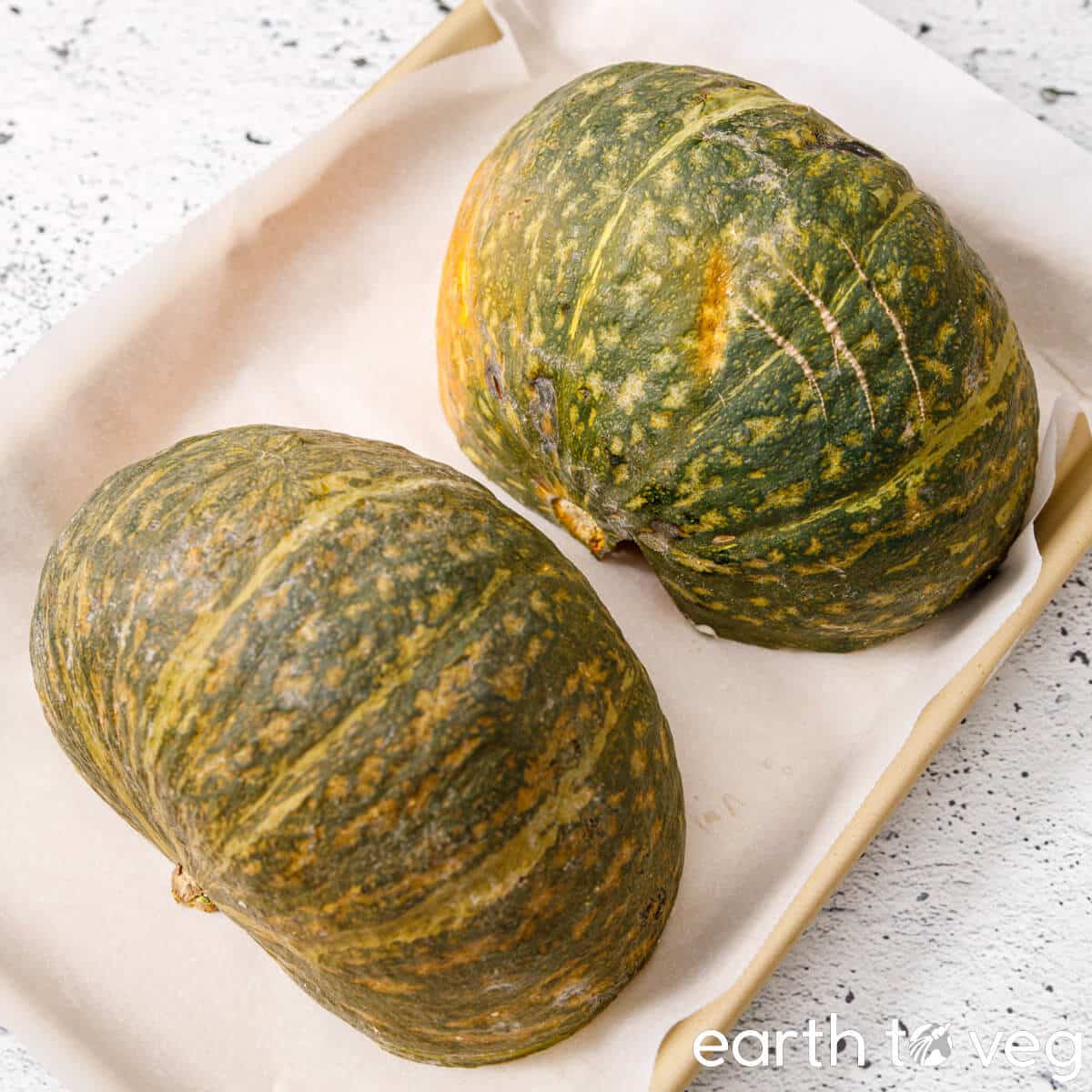 Kabocha squash halves rest on a baking pan, ready to be roasted.