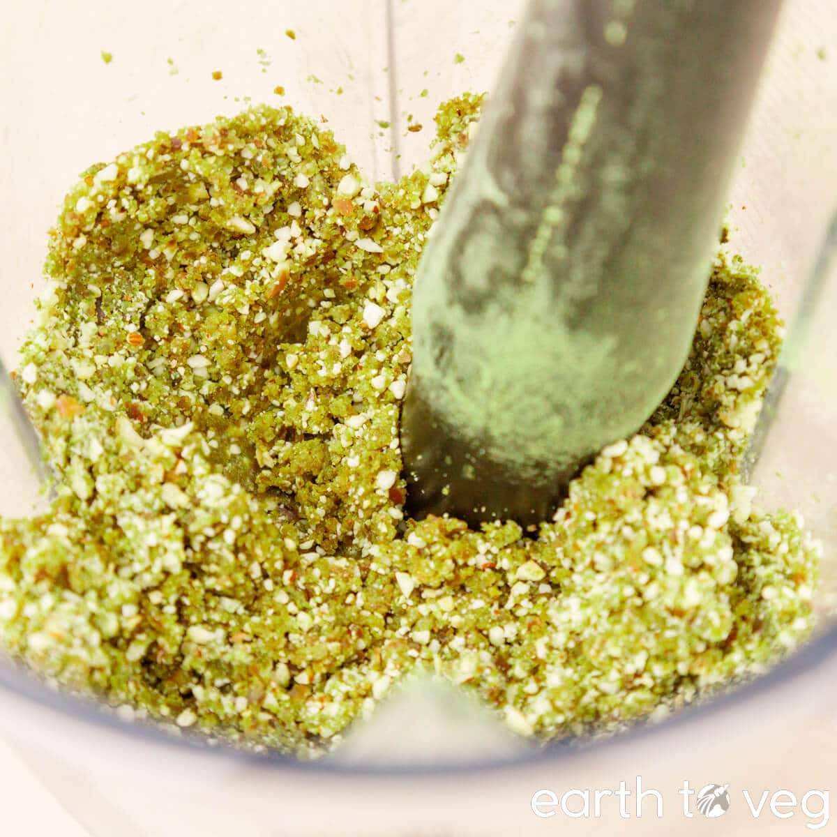 Matcha dough is pushed down with the tamper in a Vitamix blender.
