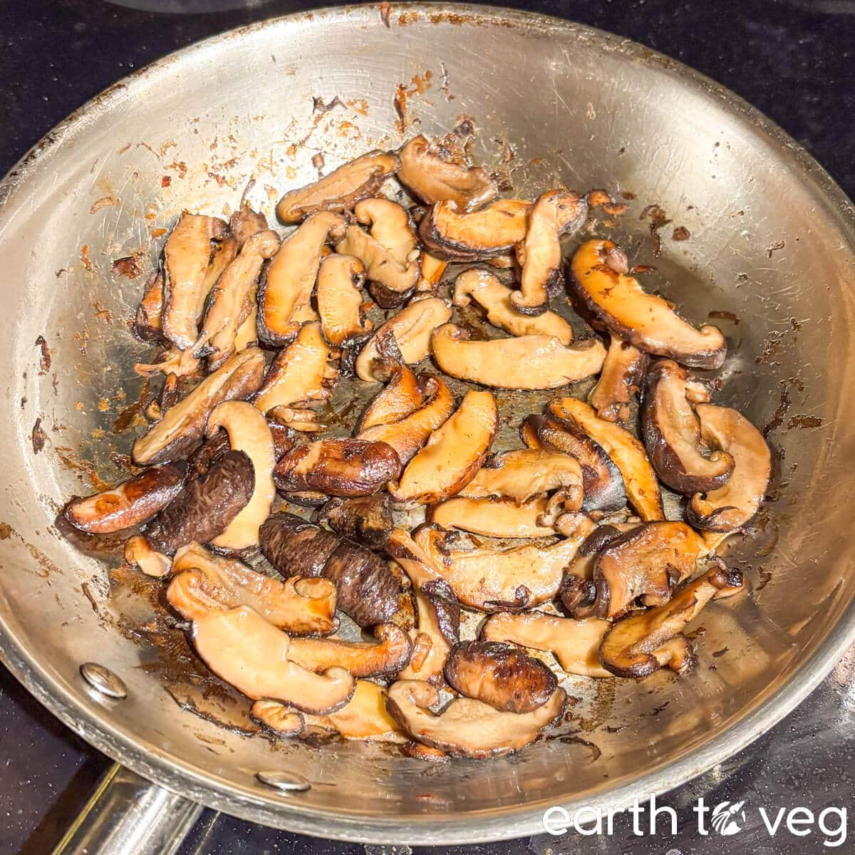 Sliced shiitake mushroom caps are sauteed in a skillet.