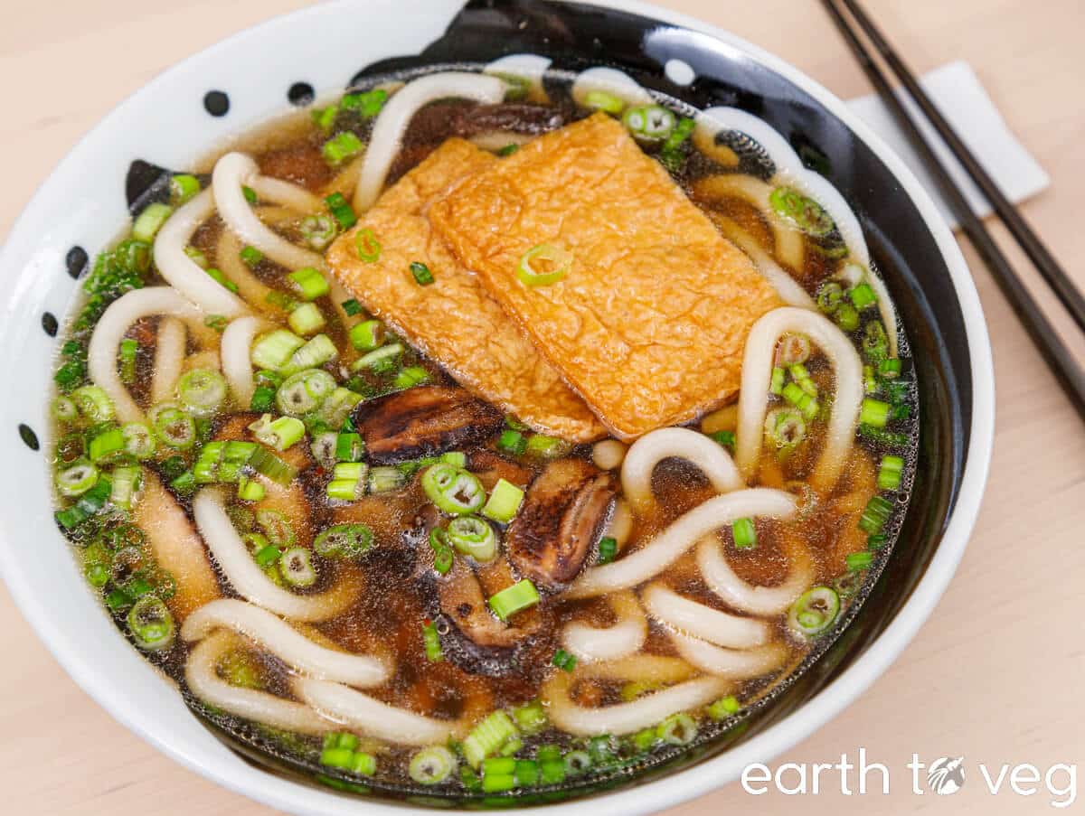 A bowl of shiitake mushroom udon noodle soup topped with abura-age (fried tofu).