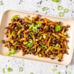 A plate of stir fried shimeji mushrooms topped with green onion.