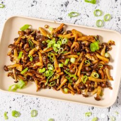 A plate of stir fried shimeji mushrooms topped with green onion.