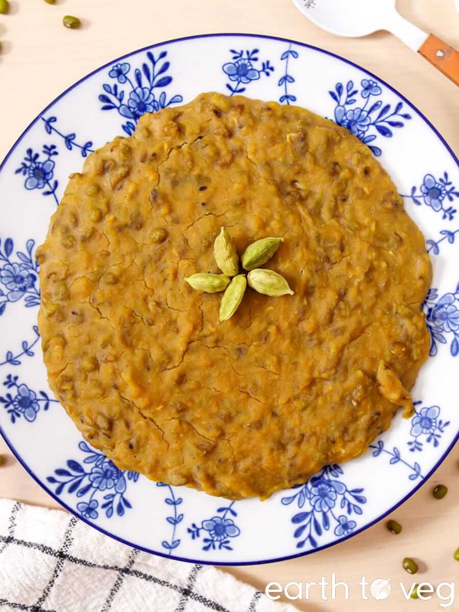 A plate of coconut mung bean pudding garnished with whole cardamom pods and shot from directly above.