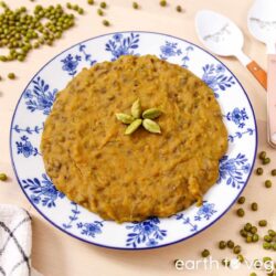 Godshe, a round Goan mung bean and coconut pudding, garnished with five whole green cardamom pods on a blue floral plate.