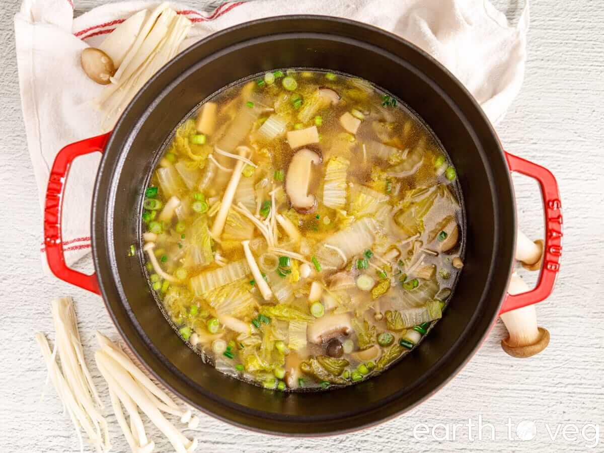 Vegetable soup in a red Dutch oven with napa cabbage, mushrooms, and scallions.