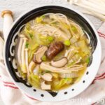 Bowl of napa cabbage soup with enoki mushrooms, shiitake mushrooms, napa cabbage, and scallions.
