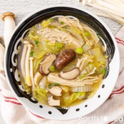 Bowl of napa cabbage soup with enoki mushrooms, shiitake mushrooms, napa cabbage, and scallions.