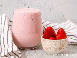 Creamy strawberry coconut smoothie served with a bowl of fresh strawberries.